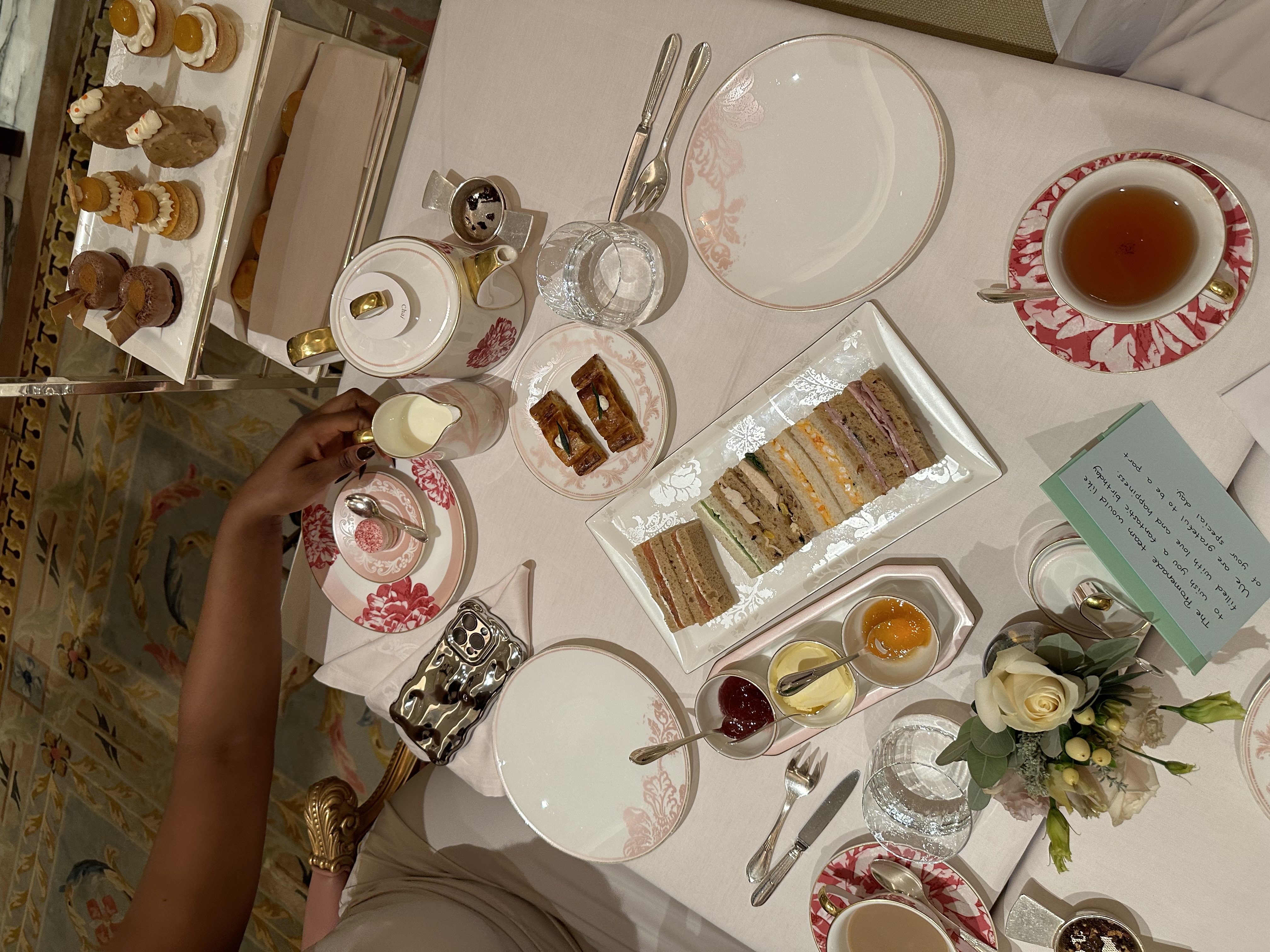 Afternoon tea at The Promenade at The Dorchester, with tea, finger sandwiches, pastries and a small floral arrangement on the table.