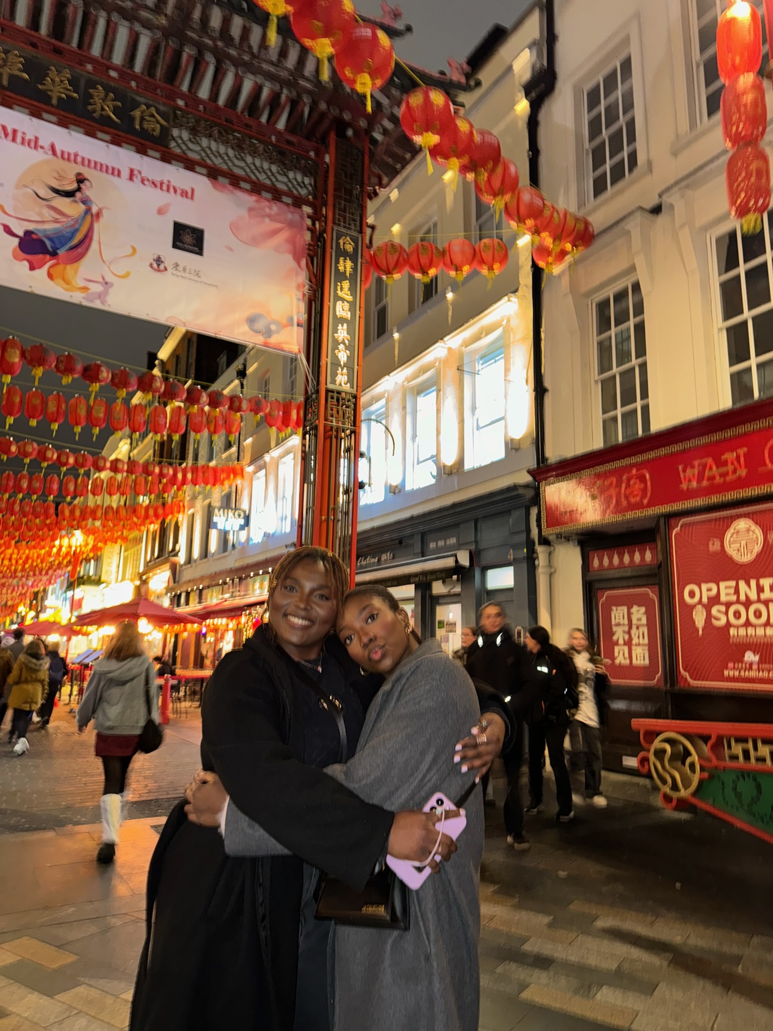 Tumininu and Ruthie embracing on a Chinatown street decorated with red lanterns.