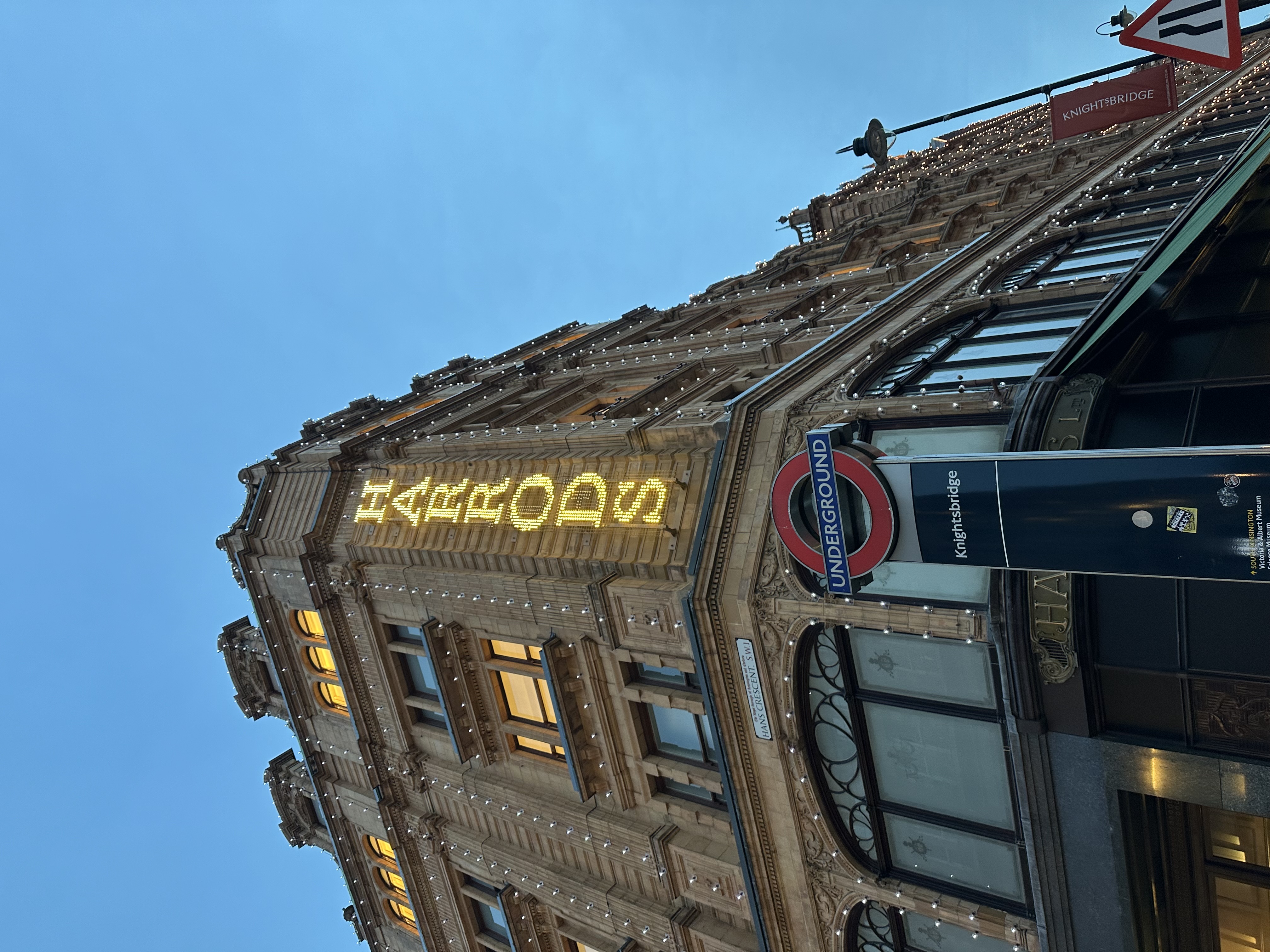 Harrods department store at dusk, viewed from street level with the Knightsbridge Underground sign in the foreground.