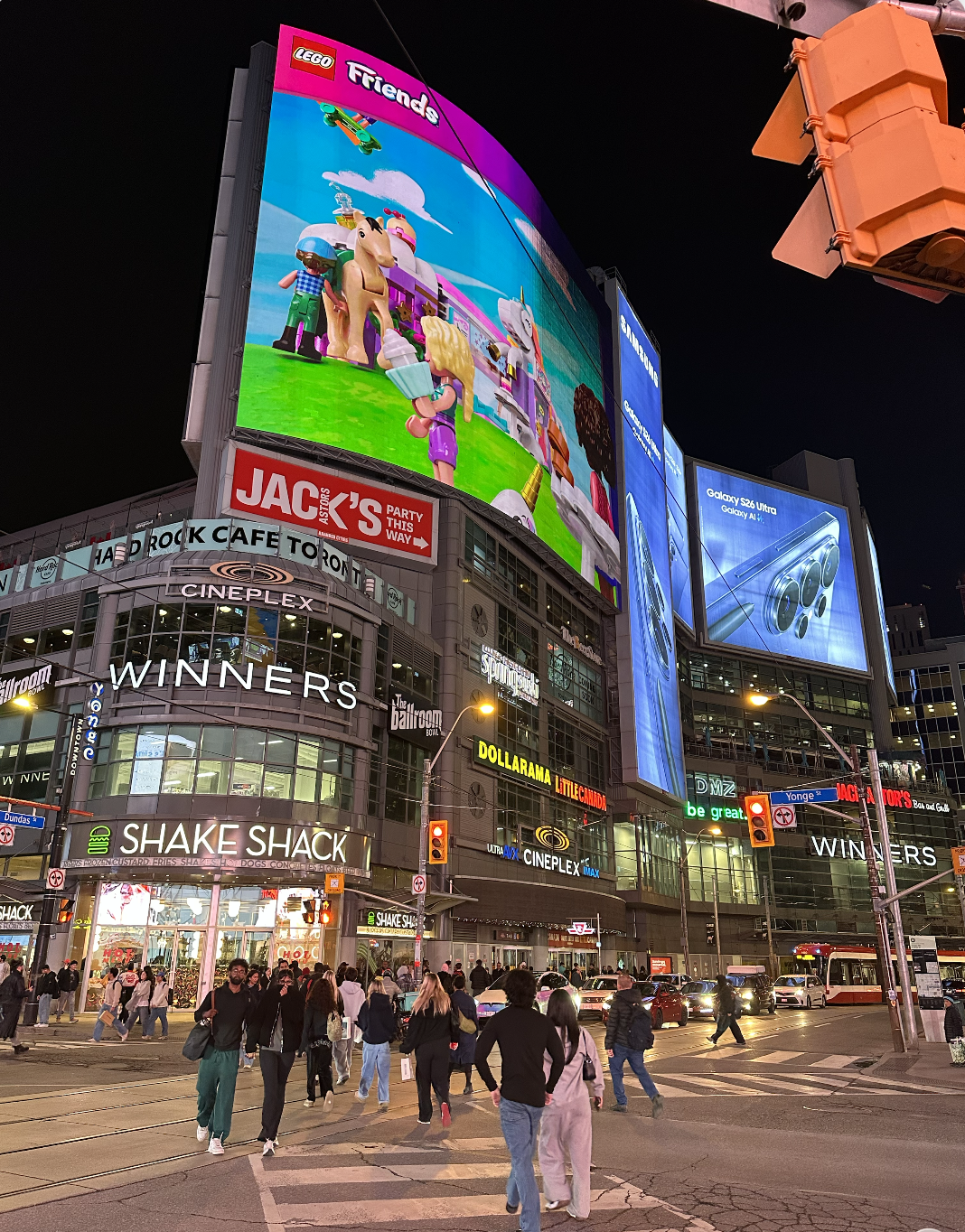 Dundas Square at night, filled with pedestrians, illuminated billboards, shops and city traffic.