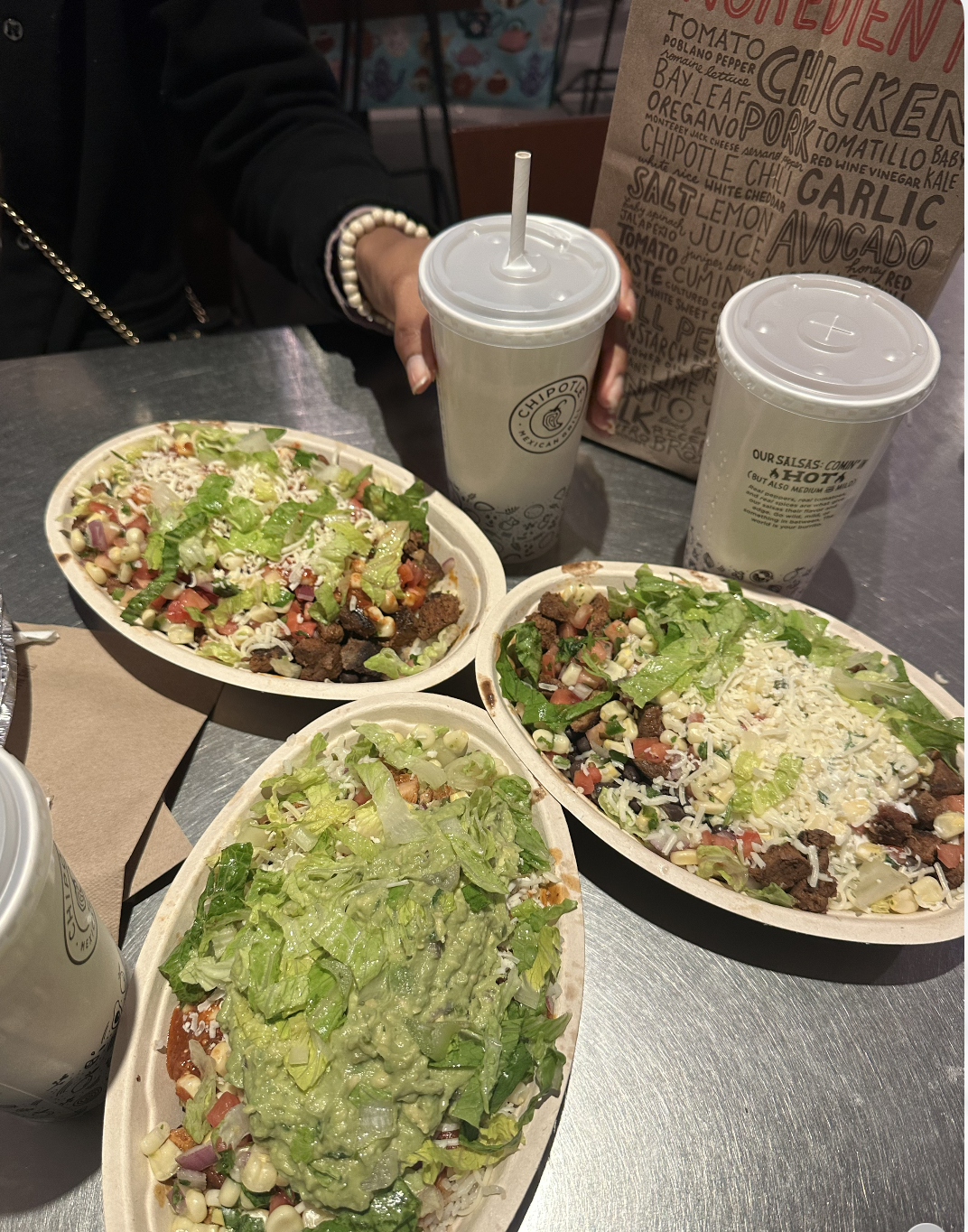 Three bowls of Chipotle food and drinks arranged on a restaurant table.